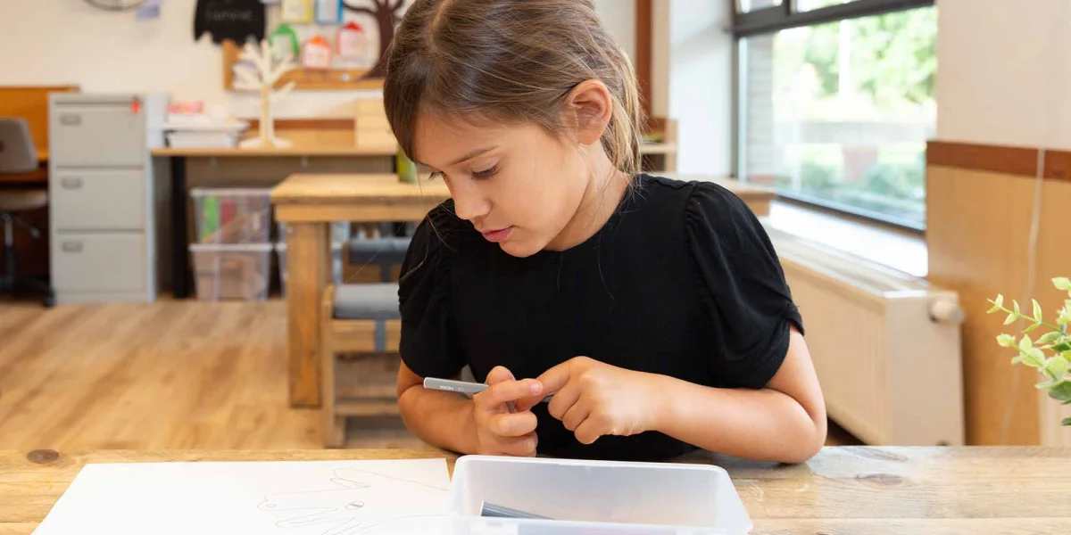 Meisje maakt tekening van hand aan tafel van kinderopvang locatie.