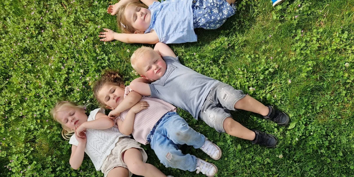 foto van 4 kinderen die in het gras liggen met een autoband er naast